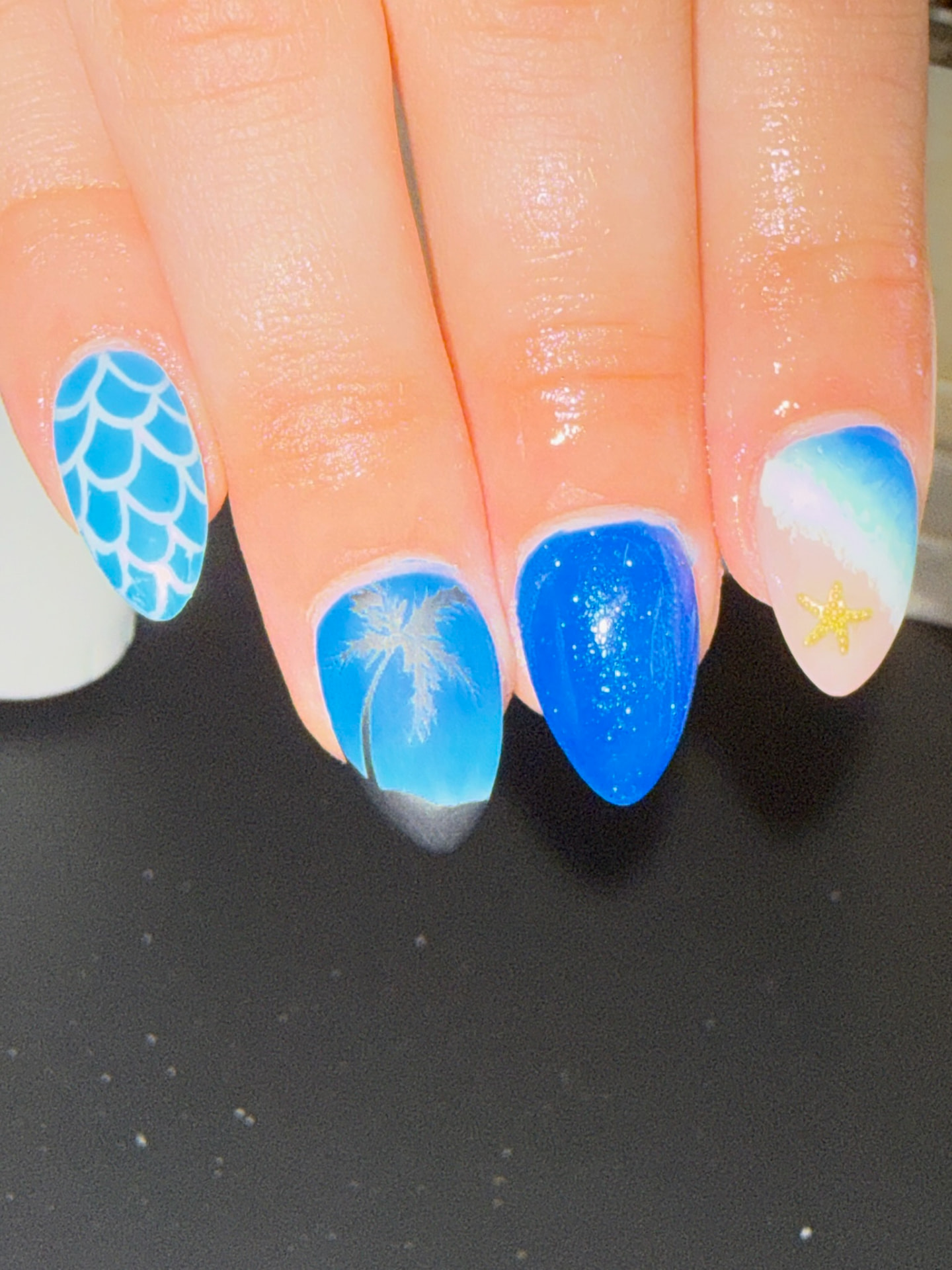 Blue beach-themed nails with waves, a palm tree and starfish art