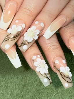 Long white French-tip nails with raised white flowers and gold accents