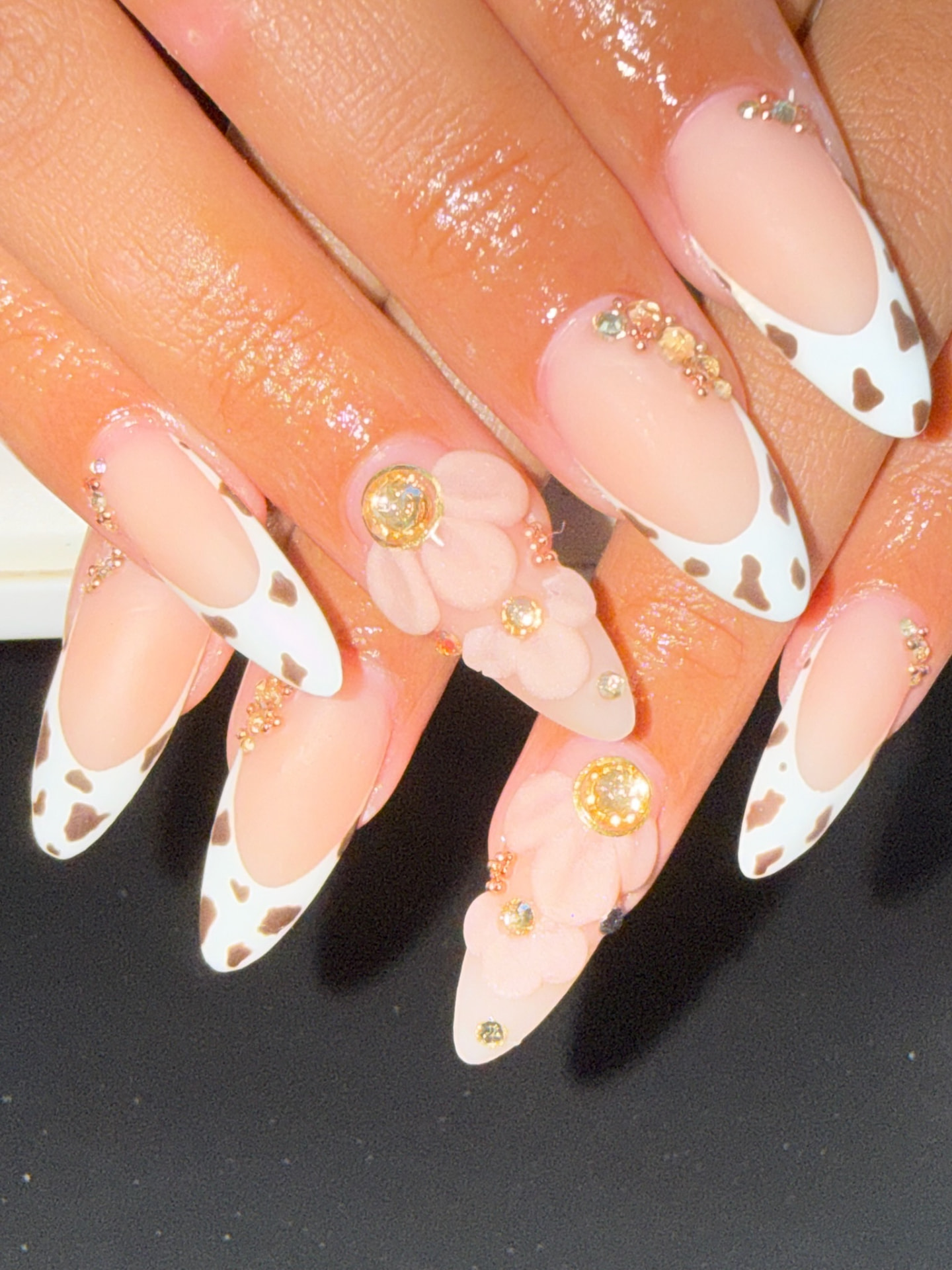 Nude almond nails with cow-print French tips, raised flowers and gems